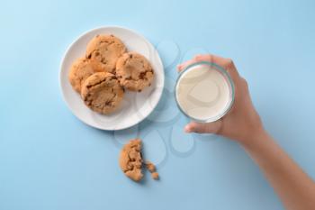 Female hand with glass of milk and tasty cookies on color background�