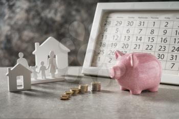 Composition with piggy bank, calendar and model of house and family on grey table. Concept of saving money for buying new house�