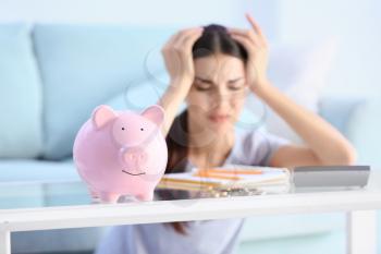 Piggy bank on table of young upset woman�