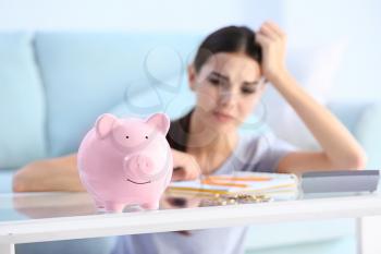 Piggy bank on table of young upset woman�