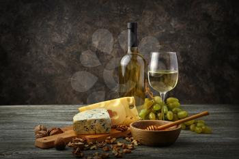 Glass and bottle of white wine with snacks and ripe grapes on wooden table�