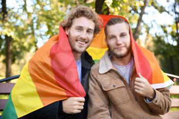 Happy gay couple with rainbow LGBT flag in park�