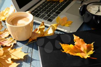 Laptop with coffee, book and autumn leaves on wooden table�