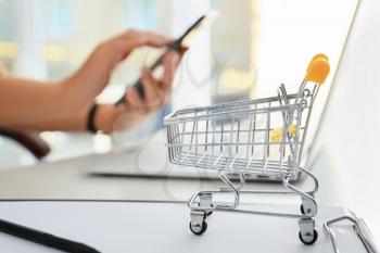 Small cart on table of woman using mobile phone and laptop. Internet shopping concept�