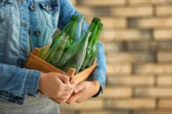 Woman holding wooden box with empty glass bottles near brick wall�