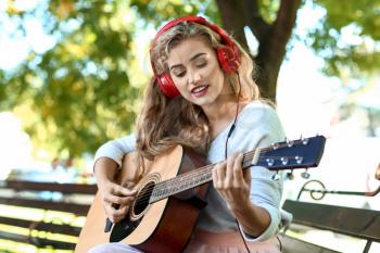 Beautiful young woman listening to music and playing guitar in park�