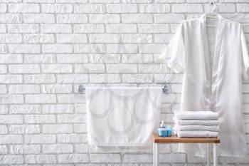 Towels with cosmetics and bathrobe near brick wall�