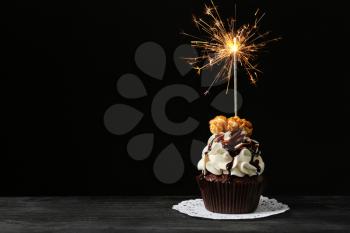 Tasty chocolate cupcake with sparkler on wooden table against dark background�