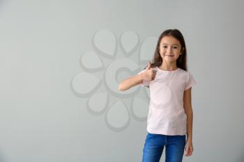 Cute girl in t-shirt showing thumb-up on light background�