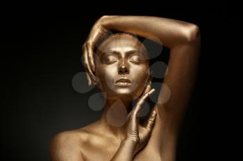 Beautiful young woman with golden paint on her body against dark background�