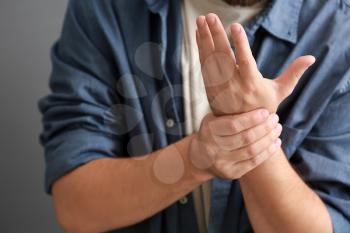 Man suffering from pain in wrist on grey background, closeup�