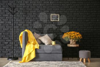 Comfortable armchair with beautiful chrysanthemum flowers near dark brick wall�