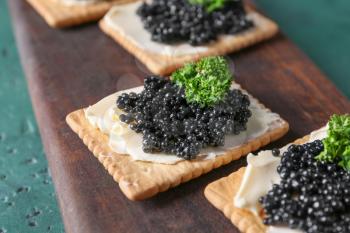 Delicious cookies with black caviar on wooden board, closeup�
