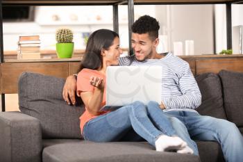 Young couple with laptop sitting on sofa at home�
