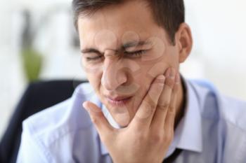 Young businessman suffering from toothache in office�