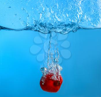 Falling of pomegranate into water on color background�