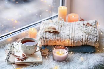 Beautiful autumn composition with burning candles and cup of tea on window sill�