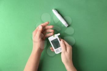 Woman measuring glucose level with digital glucometer on color background. Diabetes control�