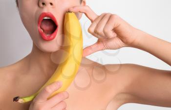 Sexy young woman with banana on light background. Erotic concept�