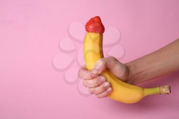 Woman holding banana with strawberry on color background. Erotic concept�