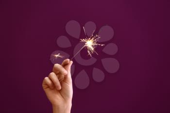 Woman holding Christmas sparkler on color background�