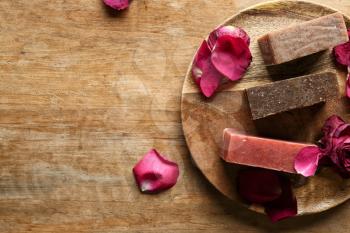 Soap bars with rose petals on wooden table�