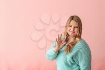 Beautiful plus size girl showing OK gesture on color background. Concept of body positivity�