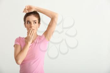 Beautiful young woman feeling smell of sweat on light background. Concept of using deodorant�