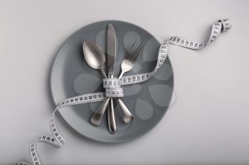 Plate and cutlery tied with measuring tape on grey background. Diet concept�