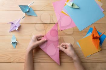 Young woman making origami on wooden table�