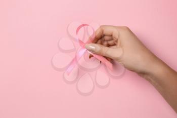 Female hand with pink ribbon on color background. Breast cancer awareness concept�