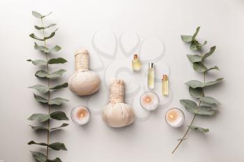 Spa composition with herbal bags, candles and essential oil on light background�