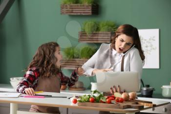 Cute daughter keeping mother from her work in kitchen at home�