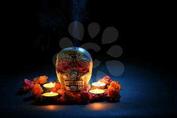 Painted human skull with burning candles and flowers for Mexico's Day of the Dead on dark background�