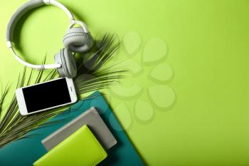 Mobile phone with headphones and stationery on color background�