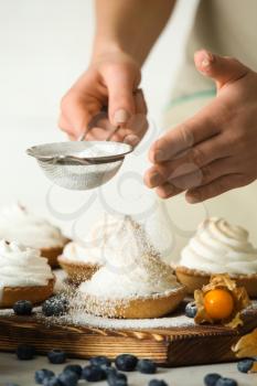 Female confectioner sprinkling sugar powder onto tasty tartlets at table, closeup�