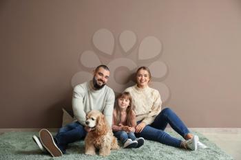 Happy family and cute dog on carpet near color wall�