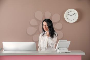 Young female receptionist talking by telephone at desk in hotel�