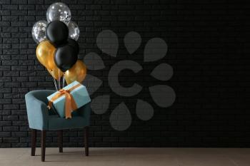 Armchair with birthday balloons and gift box in room�