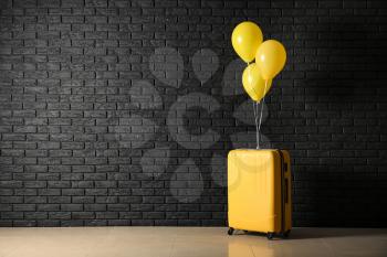 Suitcase with balloons near dark brick wall�