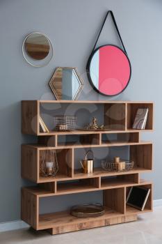 Wooden shelving unit with golden decor and mirrors on grey wall�