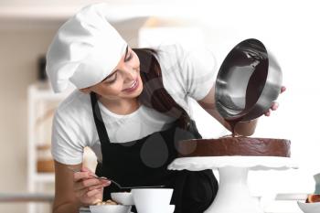 Young female confectioner cooking tasty cake in kitchen�