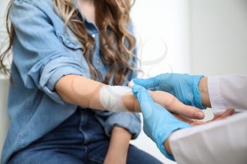Doctor applying bandage onto wrist of young woman�