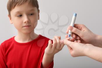 Mother taking blood sample of her diabetic child with lancet pen on light background�