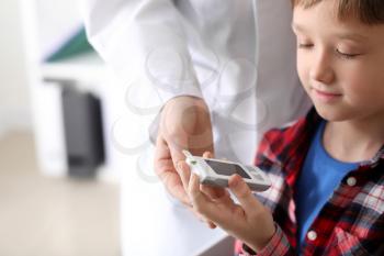 Diabetic child with digital glucometer and doctor in clinic�