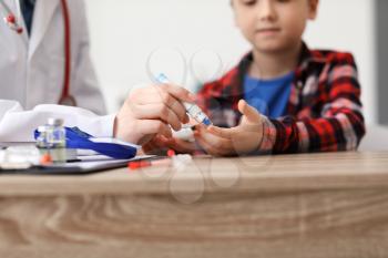 Doctor taking blood sample of diabetic child in clinic�