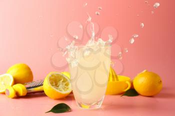 Glass of tasty cold lemonade with splashes on color background�
