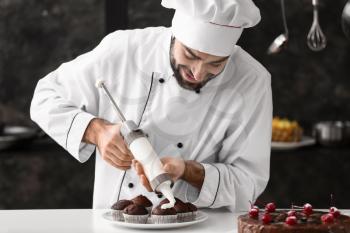 Male confectioner cooking tasty cupcakes in kitchen�
