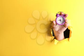 Female hand with alarm clock visible through hole in torn color paper�