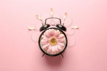 Alarm clock with flower on color background�